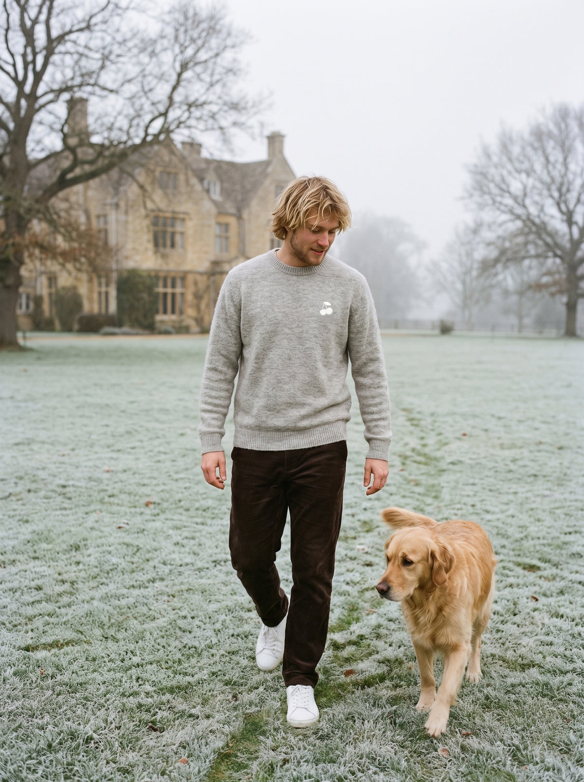A Grey Ecru crewneck with the cherry crest, worn on a frosted lawn beside a golden retriever
